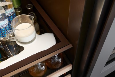 Close up of spilled glass pitcher of white creamer on nano-coated shelf of Sub-Zero 15" Designer Undercounter Beverage Center - Panel Ready (DEU1550BG)