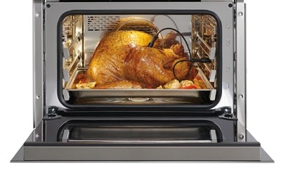 Interior view of an open Wolf 24" E Series Transitional Convection Steam Oven (CSO2450TE/S/T) displaying a perfectly cooked chicken with a probe in it