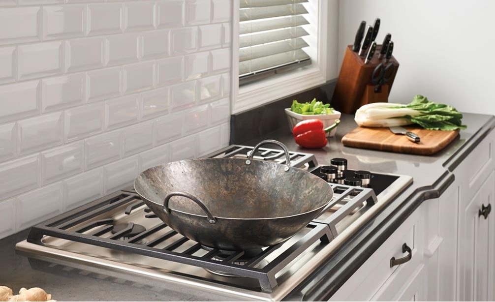 The Wolf 36&quot; Transitional Gas Cooktop 5 Burners (CG365T/S) shown set in rich granite countertop against textured white brick backsplash