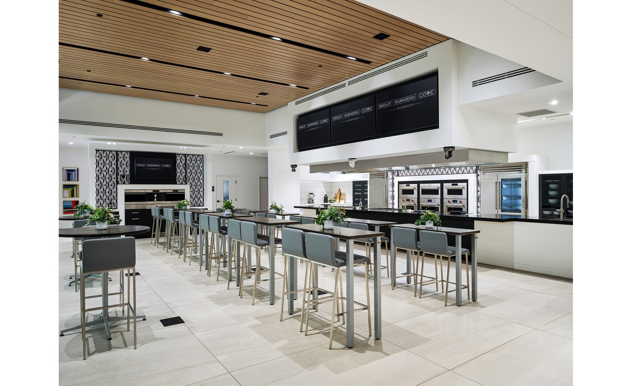 Built-In ovens by Wolf Appliances cover the walls next to a Sub-Zero refrigerator with blue-colored tall chairs.