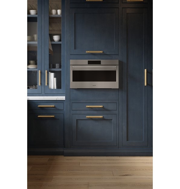 A close-up look at the Wolf 30" E Series Professional Speed Oven - SPO3050/PE/S/P built-in next to blue cabinetry