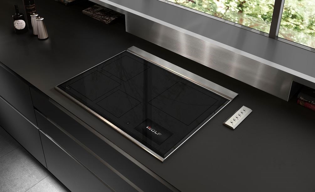 Wolf 30" Transitional Induction Cooktop (CI30460T/S) displayed in a sleek ultra modern kitchen design featuring smooth black countertops, stainless steel backsplash and handleless cabinets 