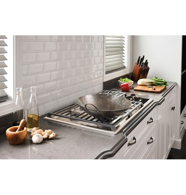 The Wolf 36" Transitional Gas Cooktop 5 Burners (CG365T/S) shown set in rich granite countertop against textured white brick backsplash