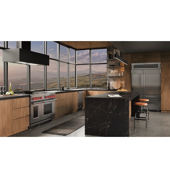 Wolf 48 Inch Professional Induction Range with matching stainless steel Sub-Zero 48 Inch PRO Refrigerator Freezer featured in an ambient  industrial kitchen design with a wall of windows overlooking an expansive mountain range.