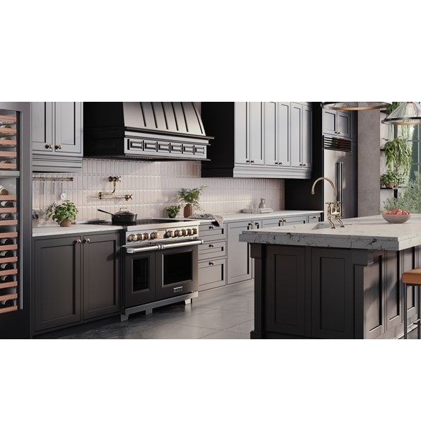 Wolf Professional Induction Range with black accent oven door and brass knobs shown in a modern bohemian kitchen design featuring custom grey kitchen cabinets enclosing a Wolf Pro Hood Liner.